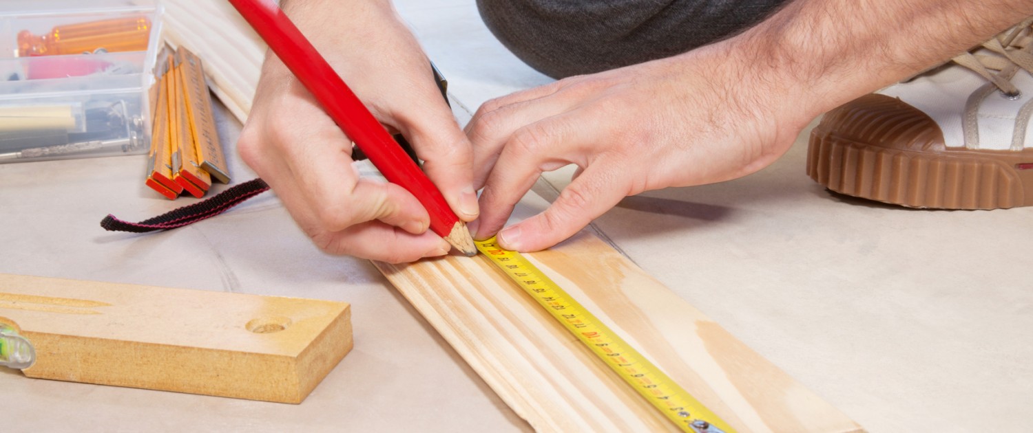 Cropped hand of a carpenter taking measurement of a wooden plank