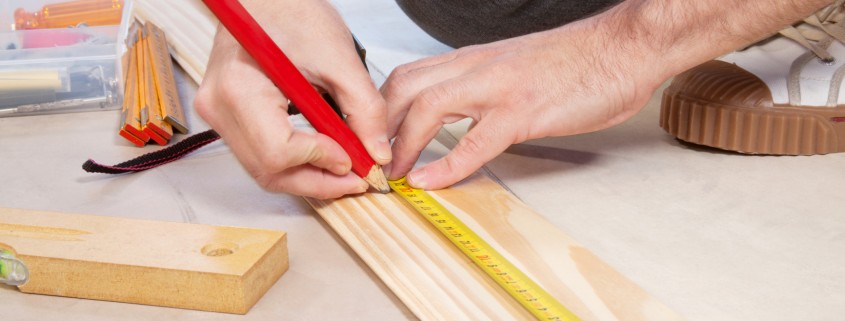 Cropped hand of a carpenter taking measurement of a wooden plank