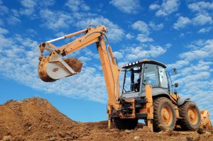 raised backhoe standing in dirt with clouds in the sky